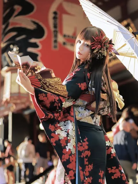 Woman holding a Japanese umbrella and showing a black floral furisode with a gold obi